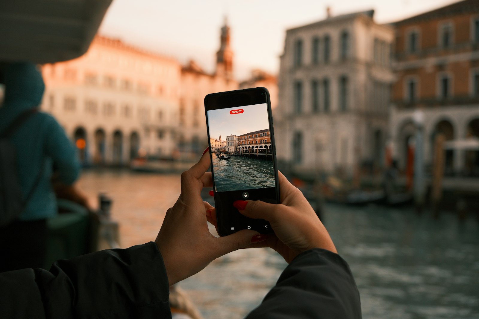 Turist filmer kanalbygninger i Italien med sin smartphone ved solnedgang